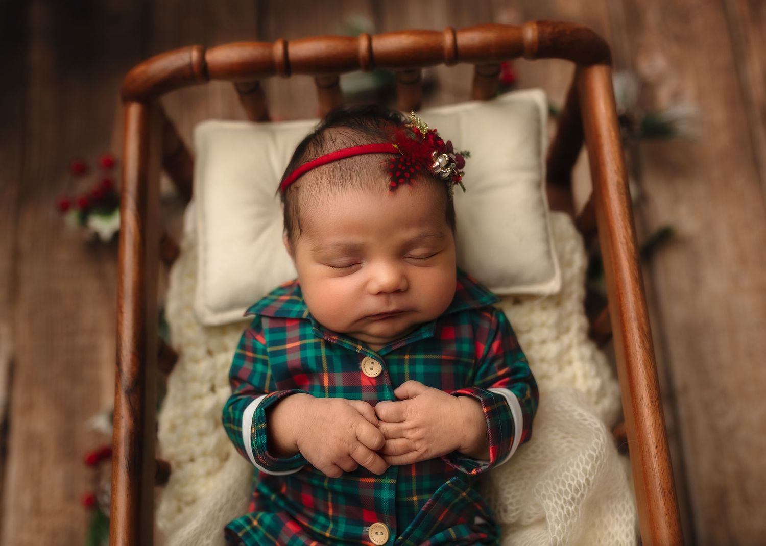 Sweet newborn girl snuggles in her Christmas jammies, sleeping in a warm wooden spindle crib, captured by Charlottesville baby photographer.