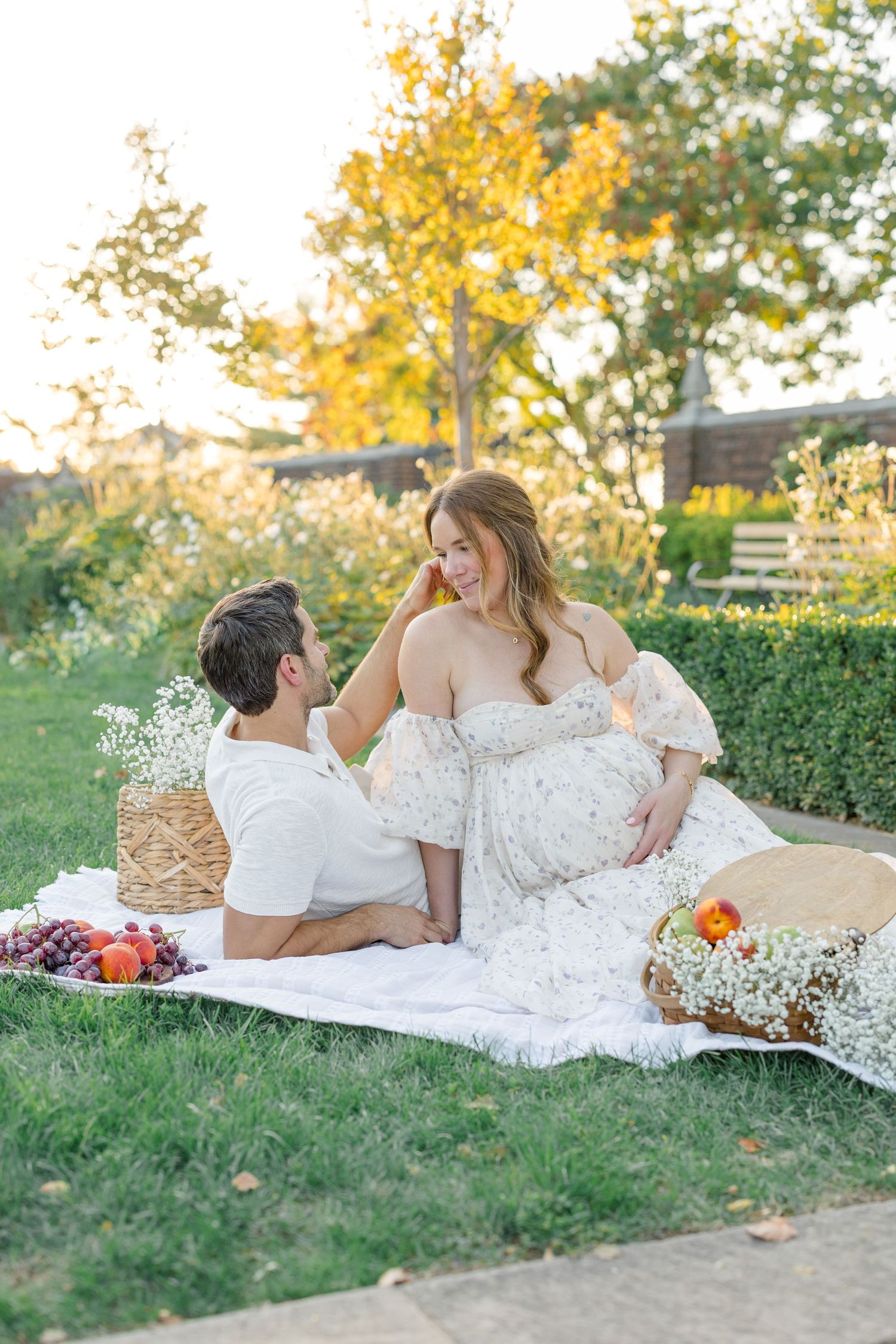 Romantic picnic scene with a white lace dress, flowers and basket on a grassy lawn at golden hour.