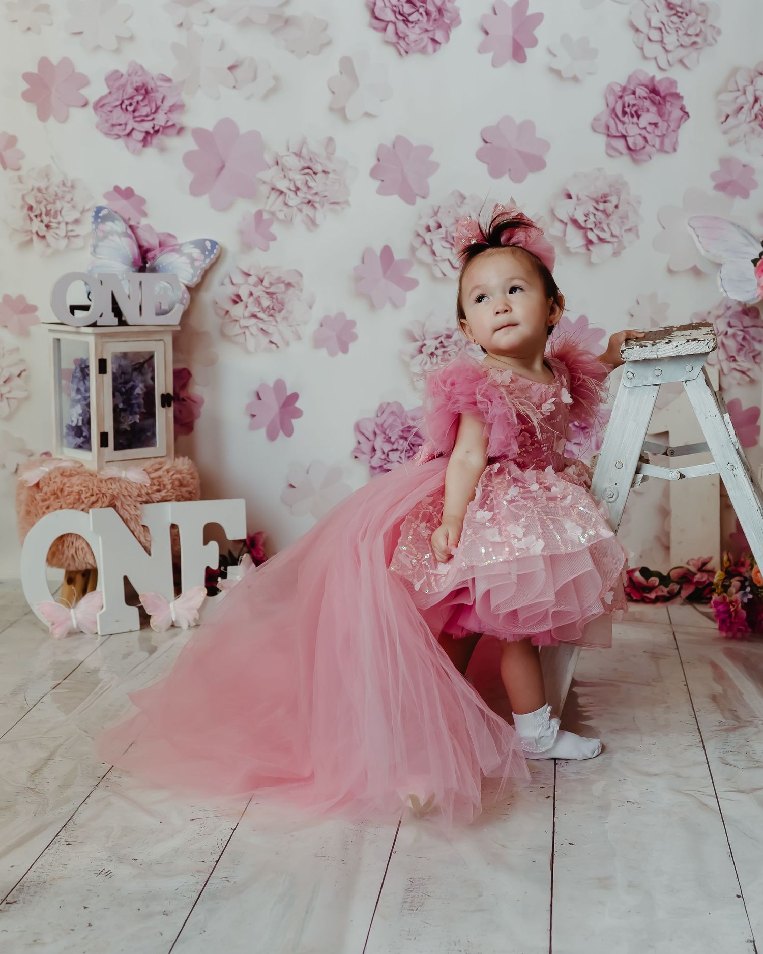 Pink tulle dress and decorative letters create a whimsical photo setup against floral wallpaper and wooden flooring.