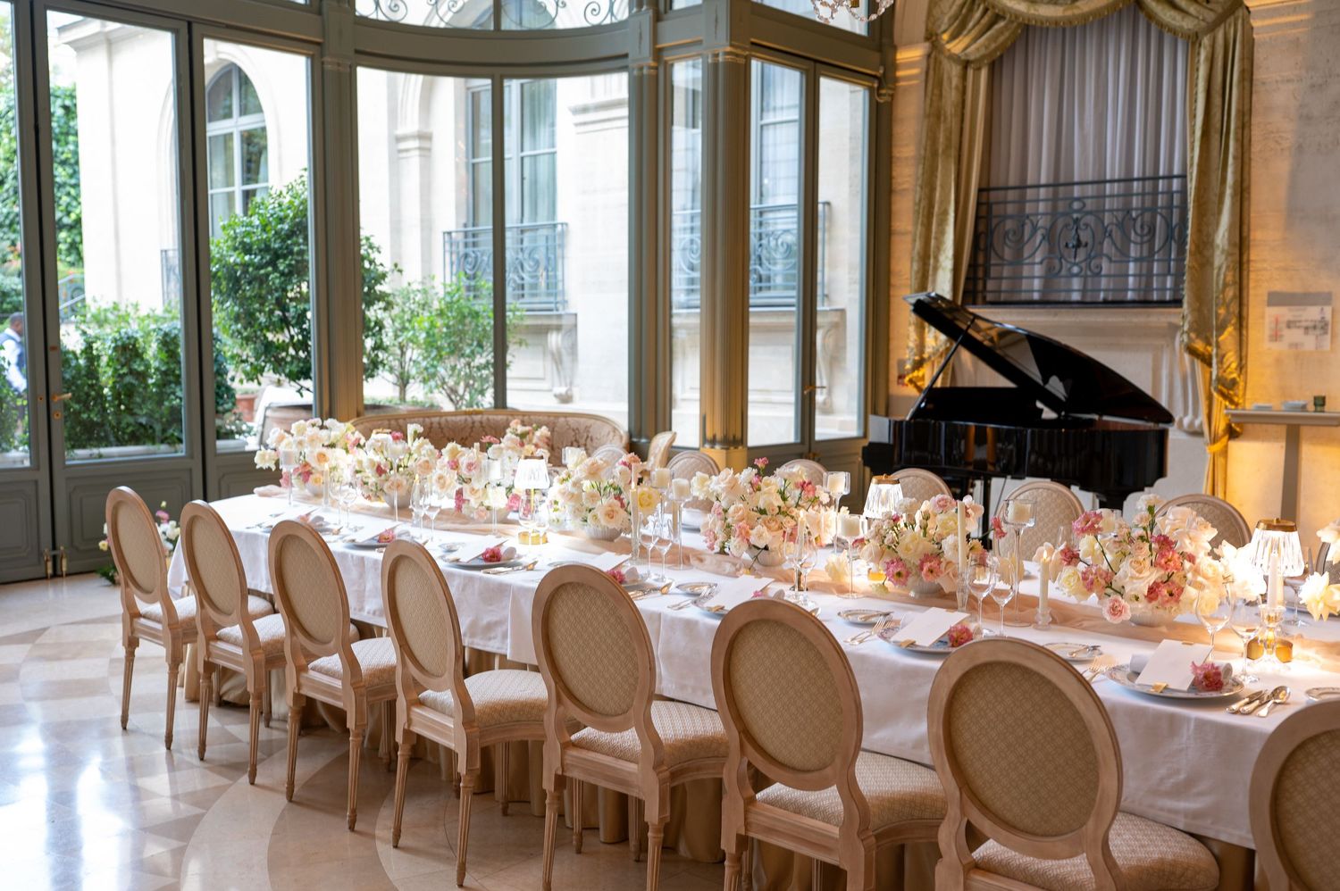 Elegant wedding reception table with white linens, gold accents and floral centerpieces in a bright windowed venue.
