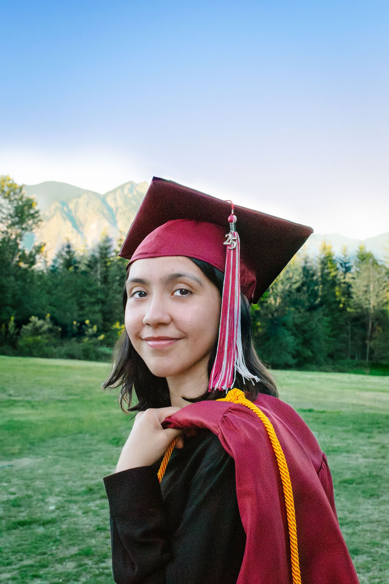 Senior girl smiling in maroon cap and gown during sunset at Snoqualmie Point Park. Seattle graduation photography.