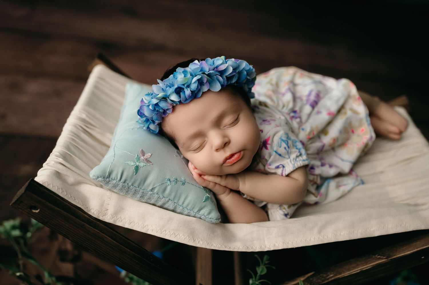Peaceful newborn sleeping sweetly on open book wearing blue floral headband and floral print outfit.
