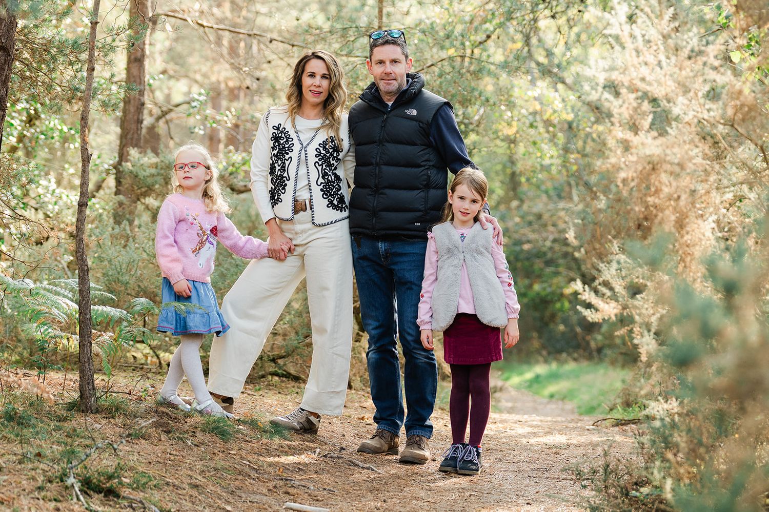 Family walking together on a sunlit wooded path during an autumn photo session.