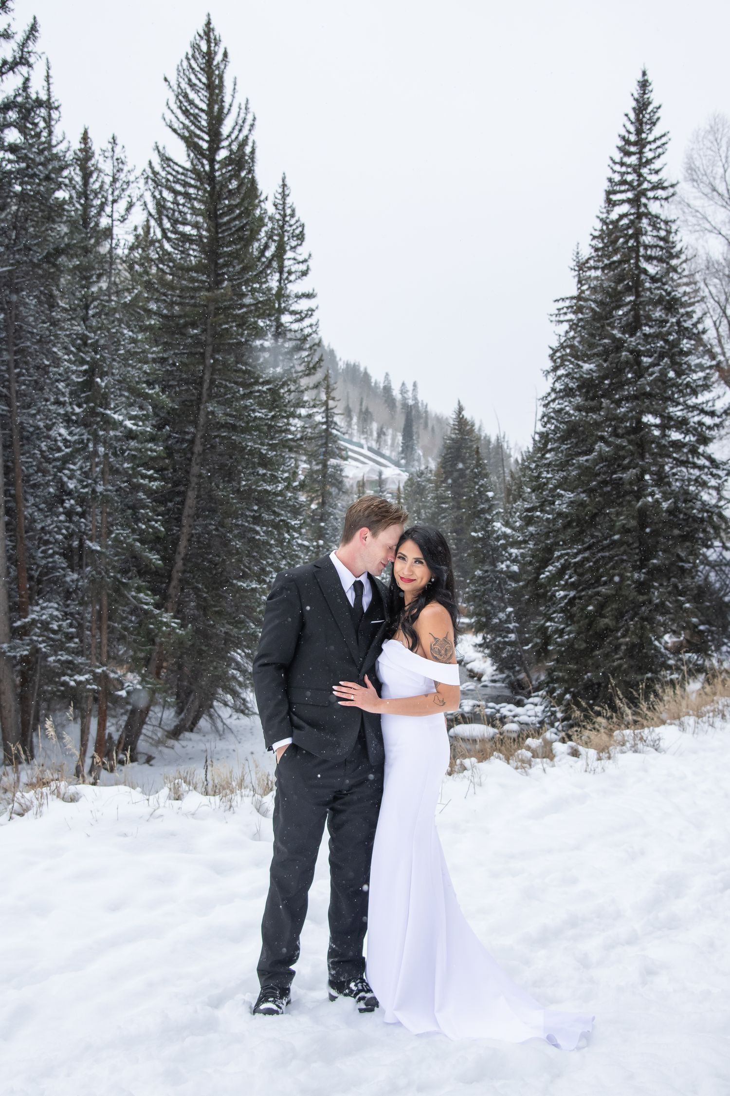 Bride and groom embraces in a snowy mountain forest setting with tall evergreen trees in the background during Vail winter wedding