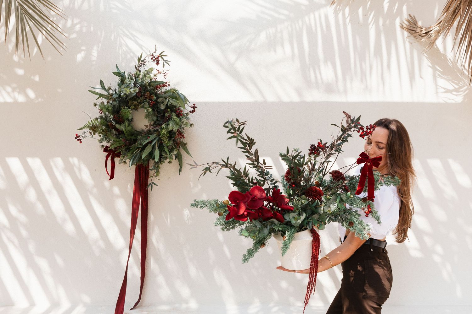 A row of festive Christmas wreaths with red bows and greenery hang on a white wall creating a holiday display.