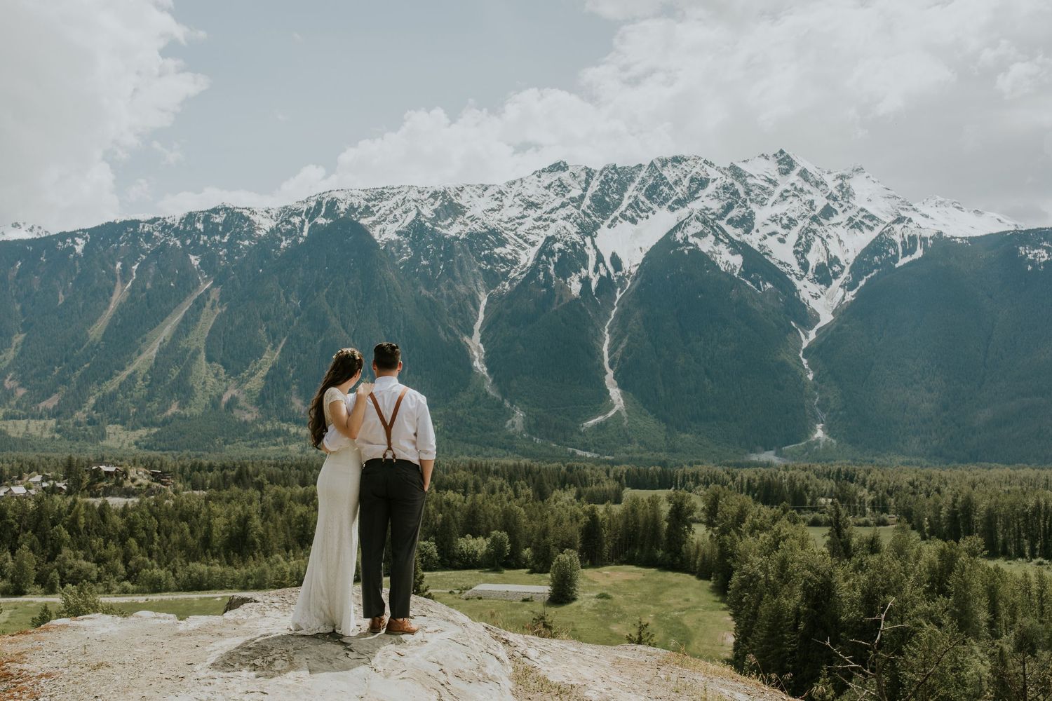 A wedding ceremony takes place on a mountain overlook with snow-capped peaks in the background.