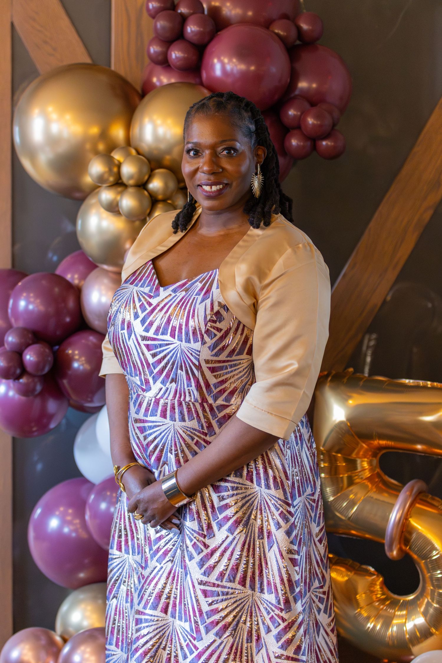 A group of guests in pink and burgundy outfits smile together during a celebration at an indoor event venue.