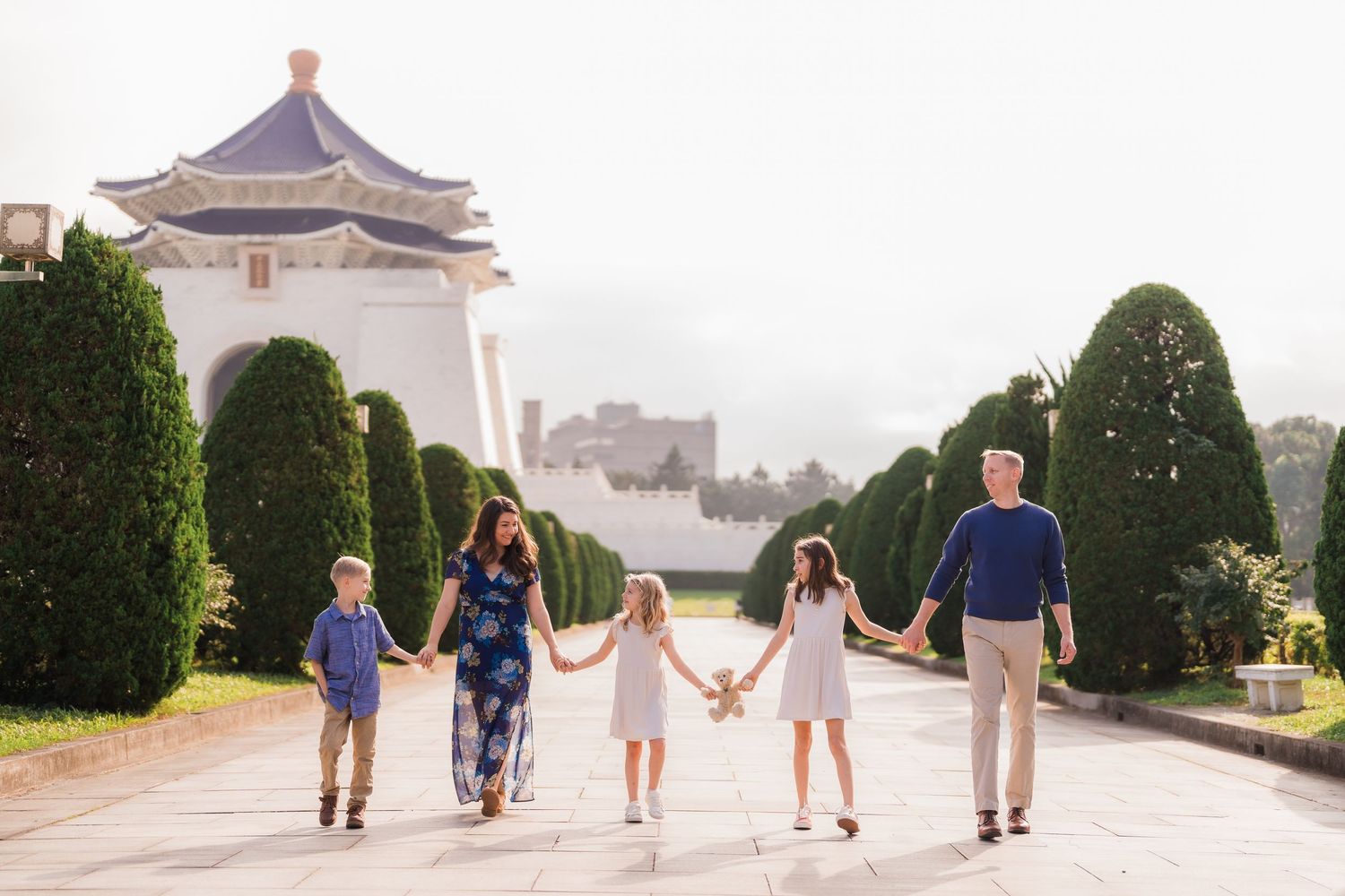 A family holding hands while walking along a path with manicured hedges and a pagoda at Liberty Memorial in Kansas City.