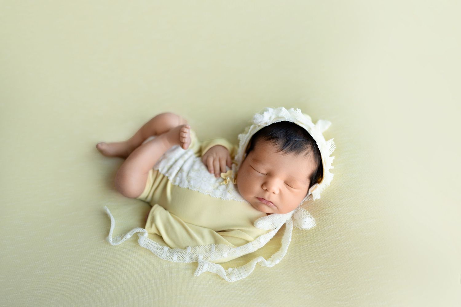 Sleeping newborn baby in soft white wrap lying in artistic posed positions against neutral beige background.
