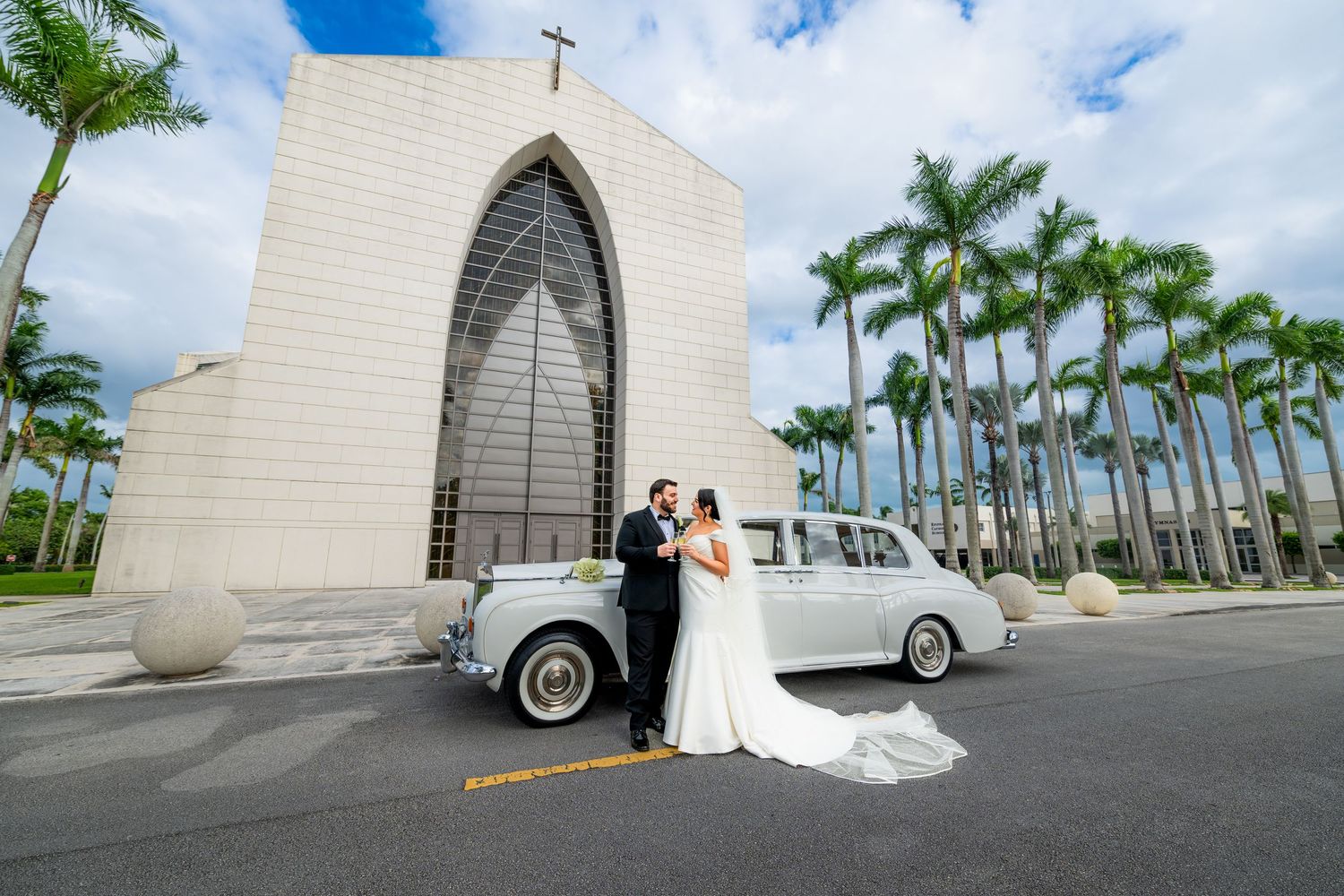 Wedding ceremony at a modern white chapel with arched entrance and palm trees against blue sky.