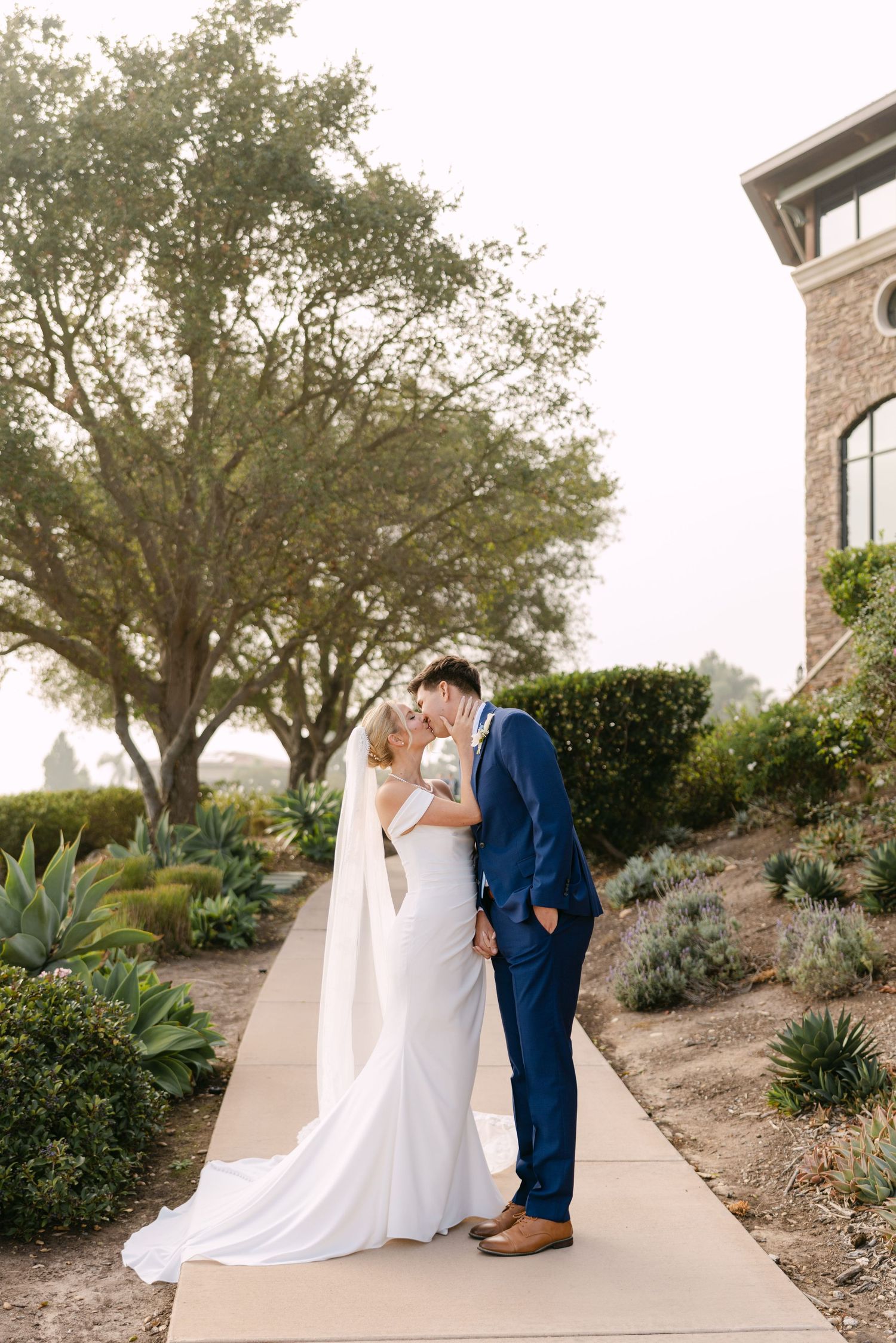 A tender moment between newlyweds posing against a white wall.