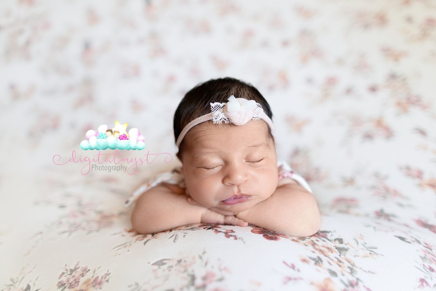 Newborn baby sleeping peacefully on pink floral backdrop wearing delicate white headband.
