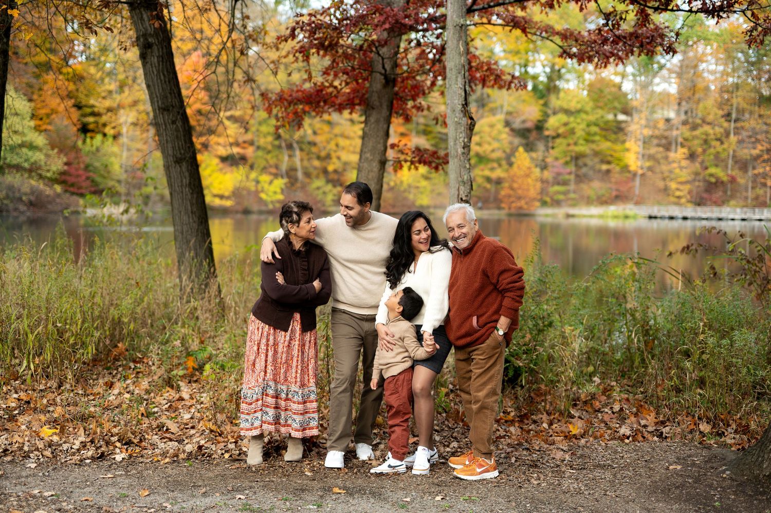 Family of four poses near a lake surrounded by colorful autumn foliage.