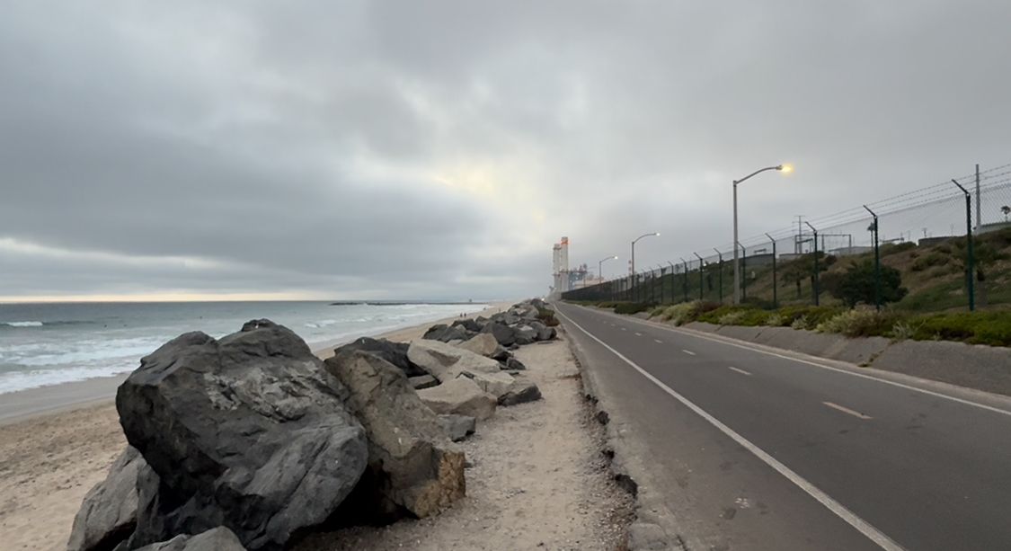 Winding coastal road curving along rocky shoreline under moody cloudy sky at sunset.