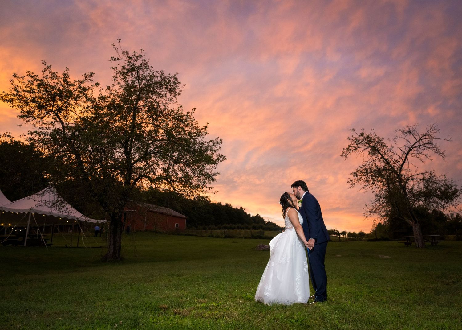 Newlyweds share an intimate moment by a brick garden wall at sunset.