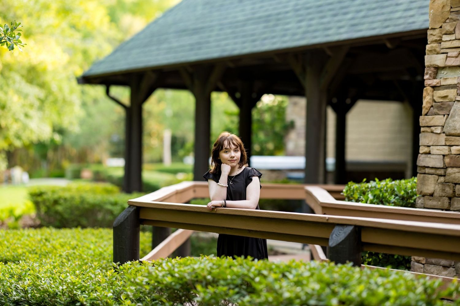 Covered bench area in garden setting with stone pillars and green landscaping.