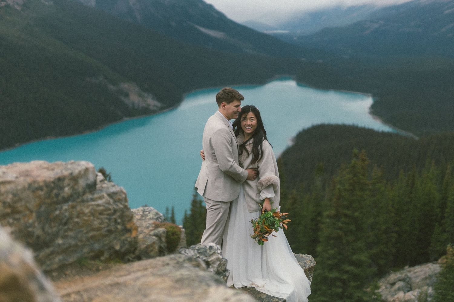 bride and groom cuddle on a rocky outcrop above Peyto Lake in Banff National Park