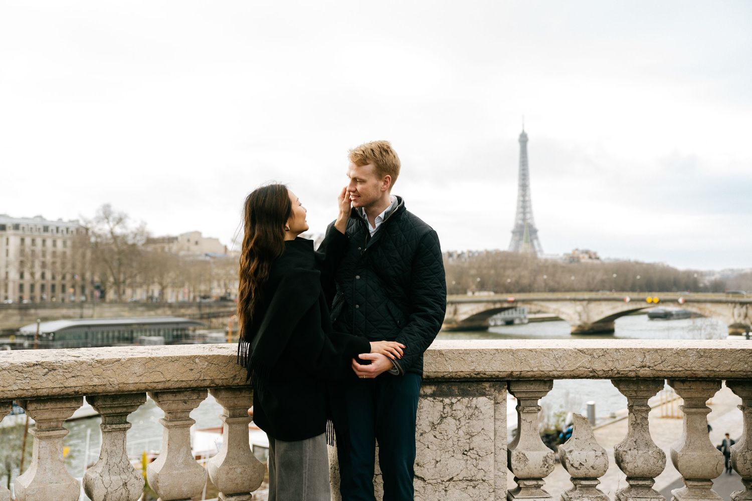 A couple shares a romantic moment on a stone bridge overlooking the Eiffel Tower in Paris.
