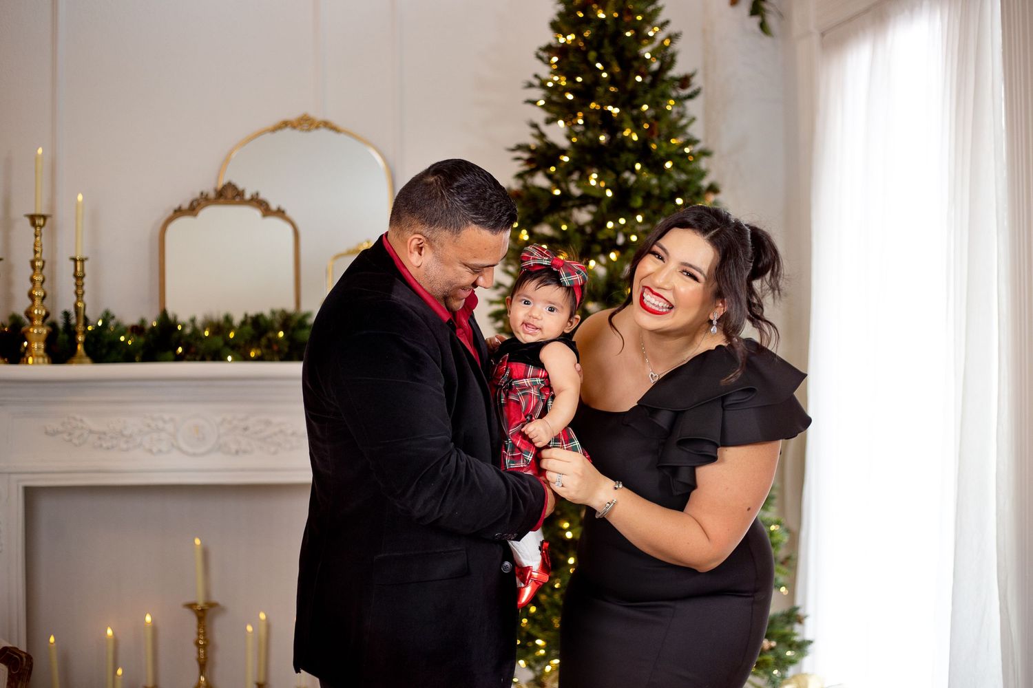 Family shares a joyful moment together by their decorated Christmas tree and mantle with glowing candles during holiday photoshoot.
