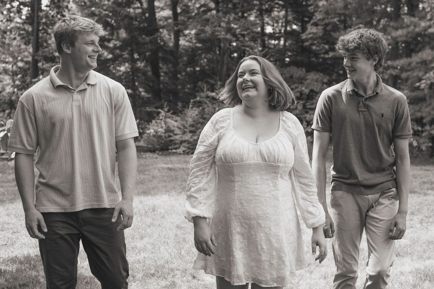A black and white photograph showing three young adults walking and laughing together outdoors in a natural setting.