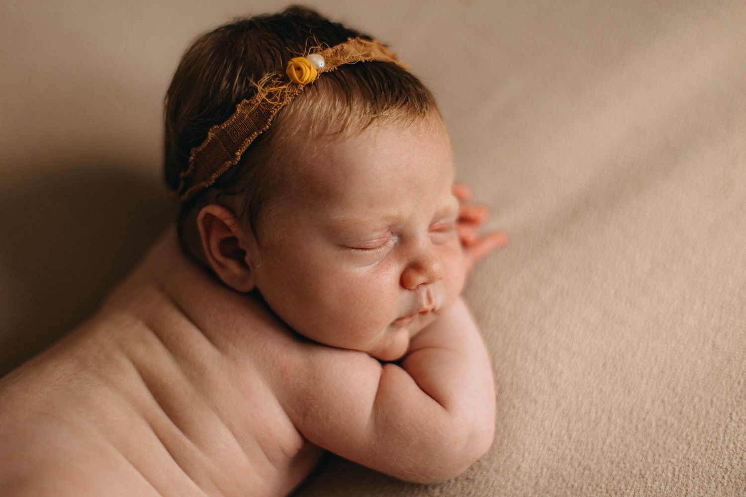 Sleeping newborn posed with orange fabric in studio setting.