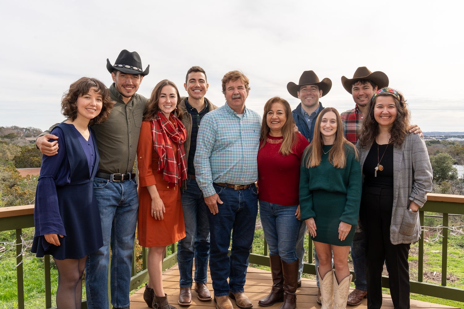 Group of people in casual western wear standing together on an outdoor deck with scenic view.