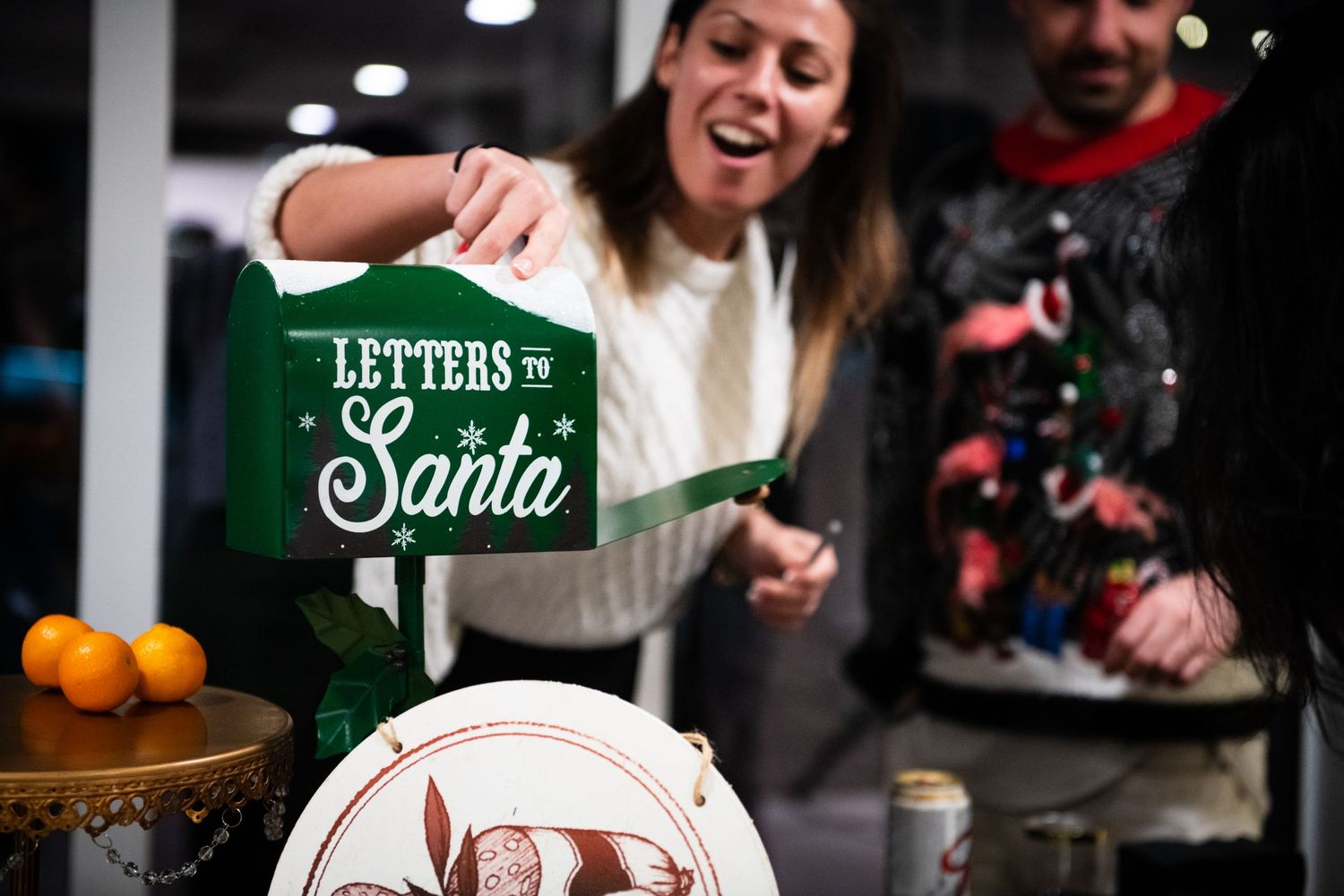 People placing letters to Santa in a festive green mailbox during holiday season.