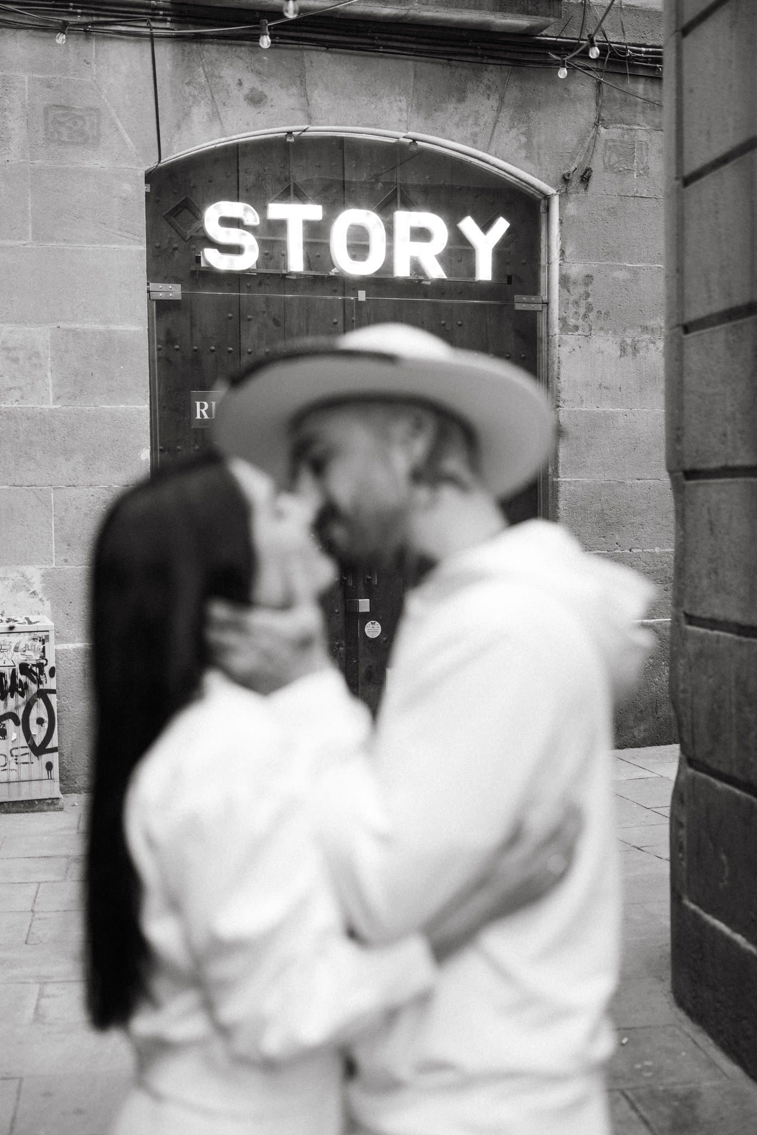 Black and white photo of a couple dancing in front of a wall with a 'Story' sign.