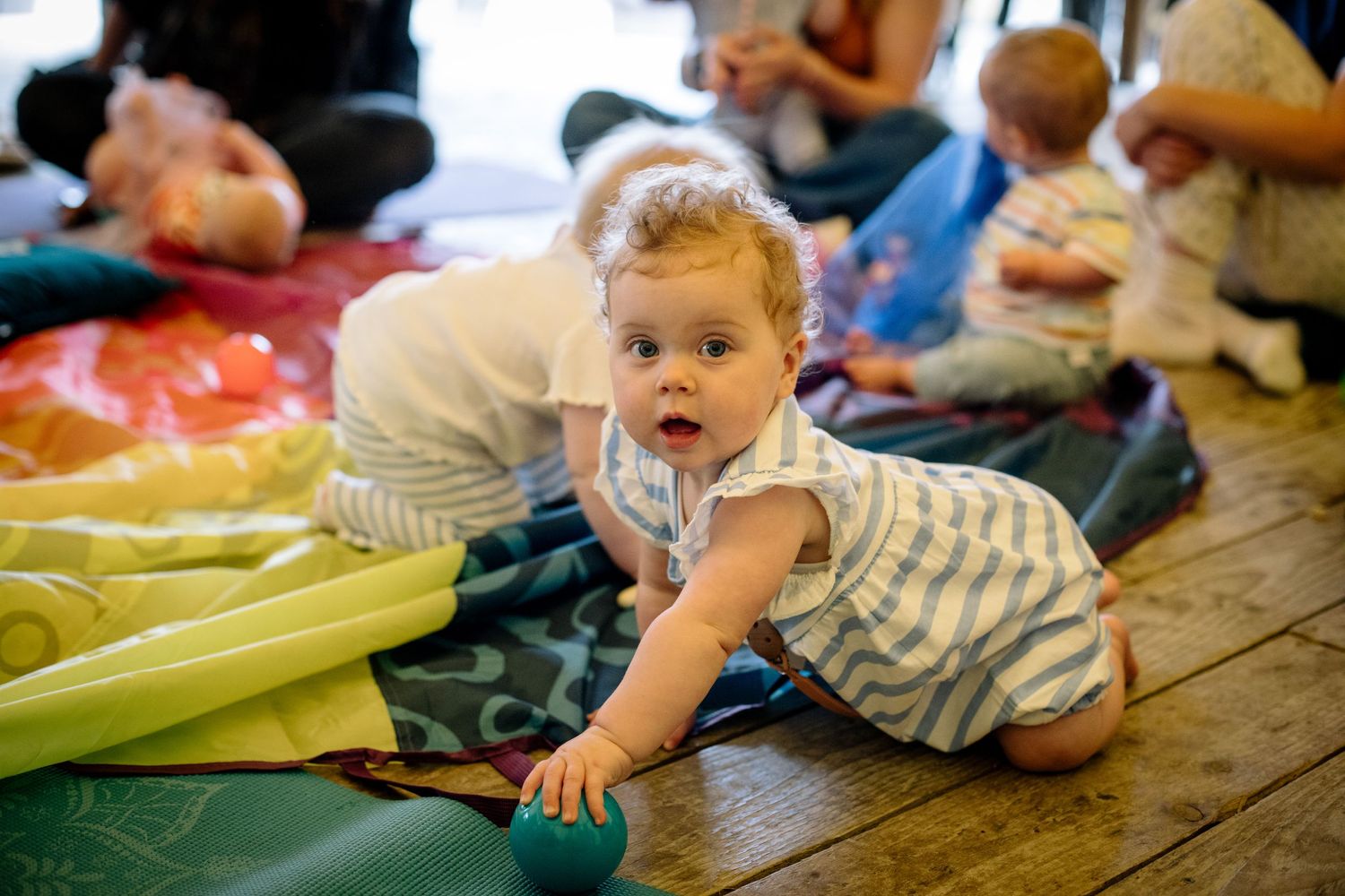 Baby in striped clothing crawling on colorful floor mats during playtime.