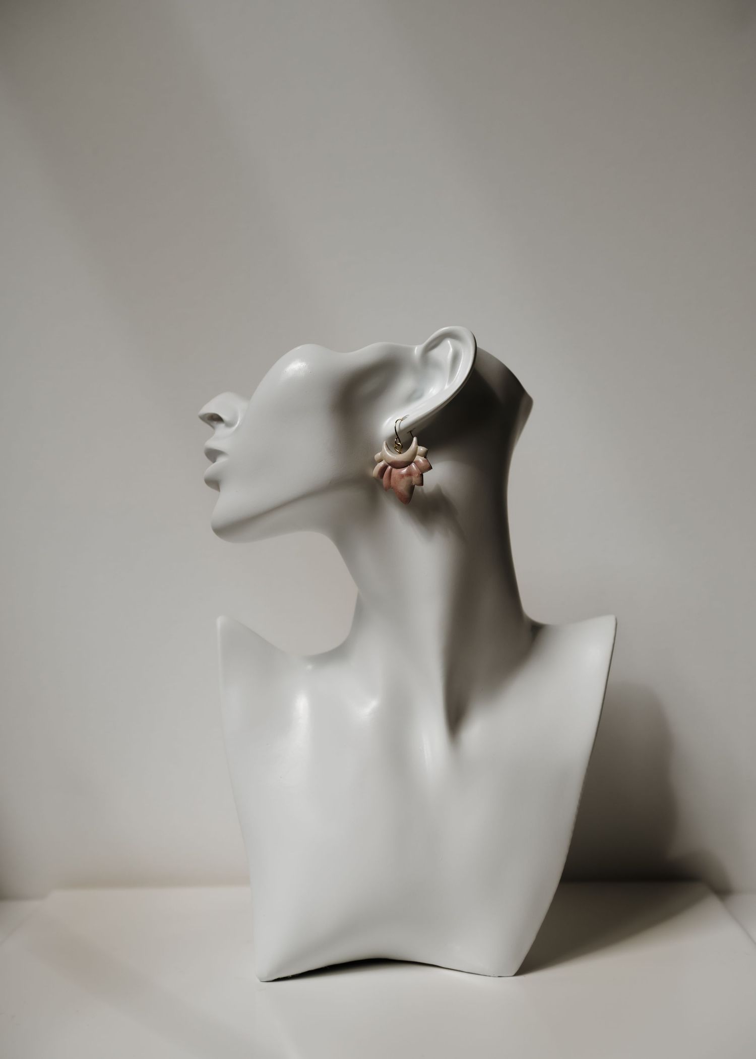 A white jewelry display mannequin bust turned to the side with a delicate pearl and gold earring against neutral background.