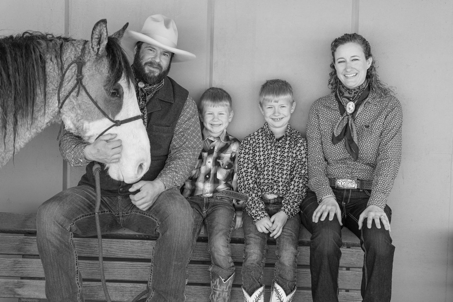 Black and white western family portrait with a horse sitting on wooden bench together.