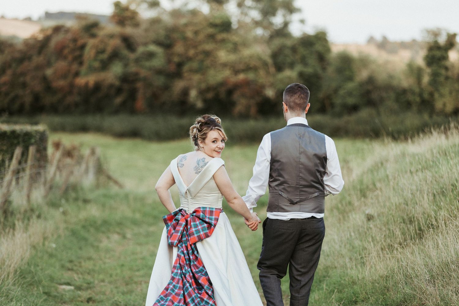 Couple walking together in a grassy meadow with the person in a white dress with colorful overlay walking behind. 📌 Pin this photo