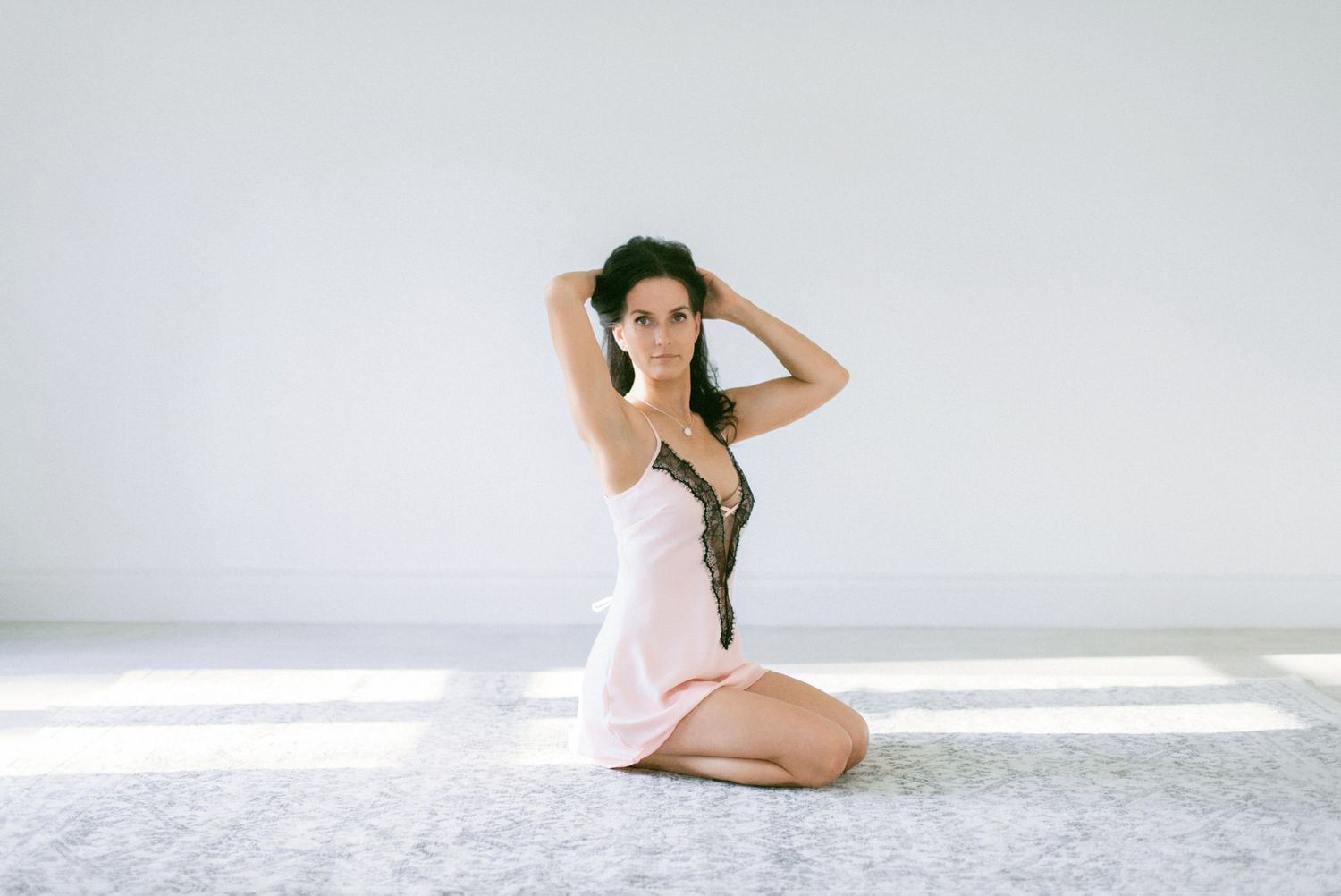 Person in a green cap and light dress sitting gracefully on a minimalist white floor with natural lighting.