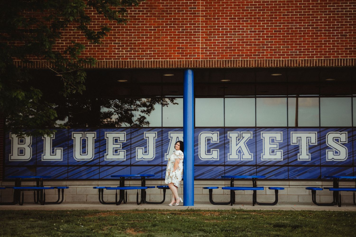 A blue metal pole stands in front of Blue Jackets athletic facility text with brick wall and benches.
