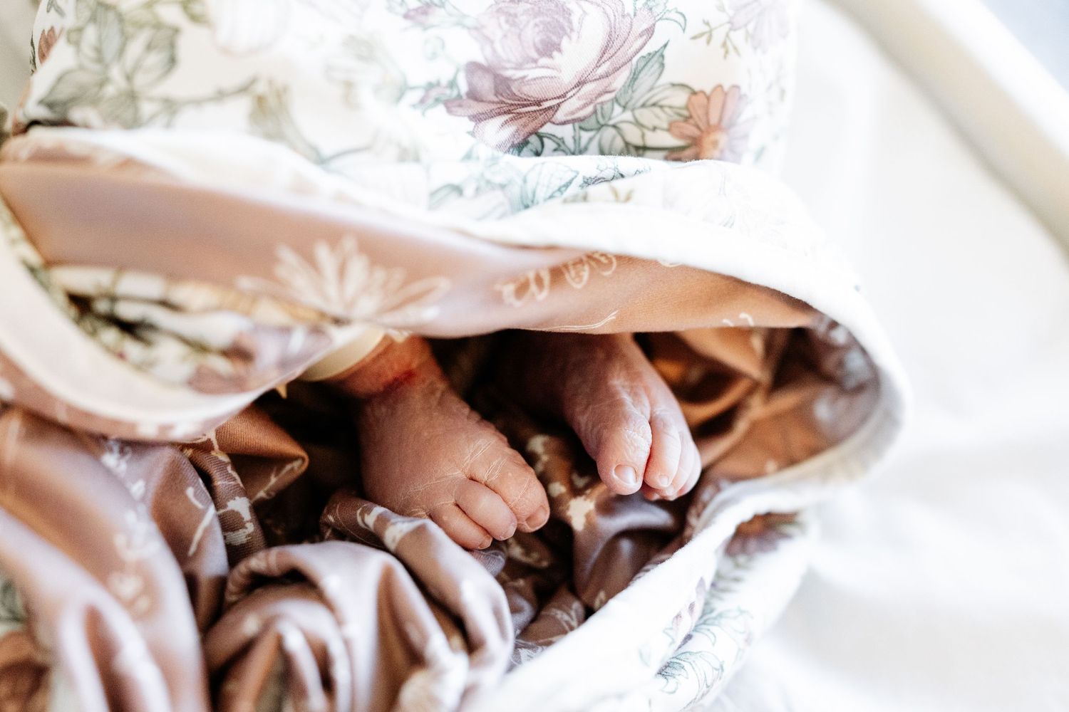 A close-up view of cozy feet tucked under a soft brown blanket on white bedding.