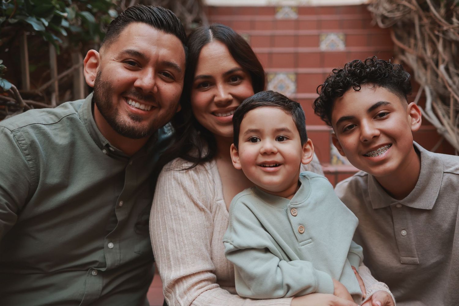 Family of four posing together for a close-up portrait against brick wall backdrop.