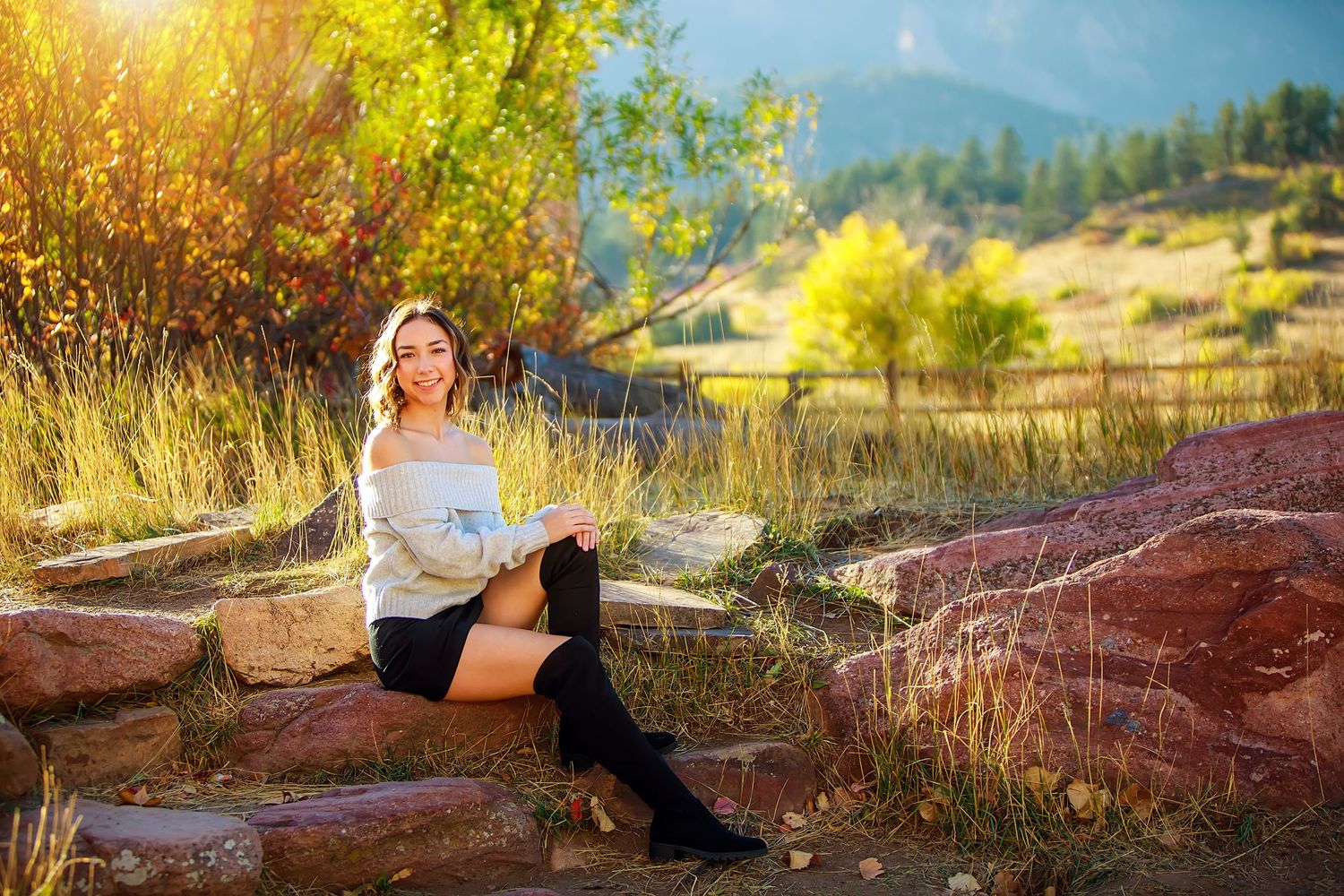 Person in casual outfit sitting on red rocks with mountain landscape in background.