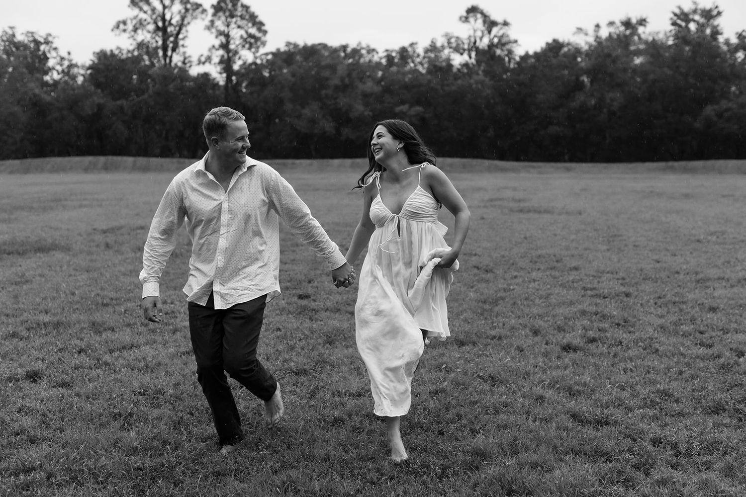 A couple holding hands and running through a grassy field in black and white photography.