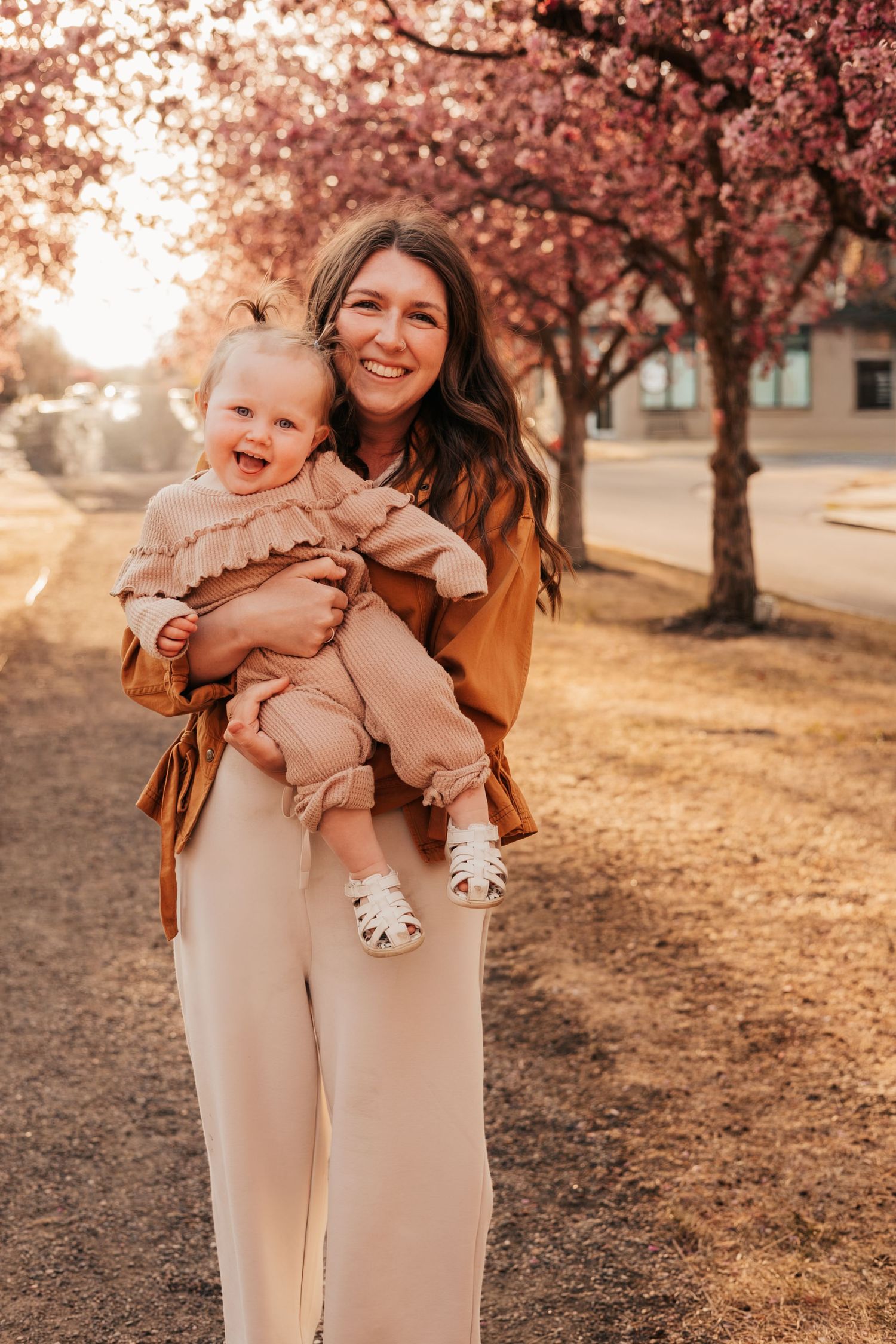 Smiling mother holding happy baby girl among pink cherry blossom trees | How to Get Nice Family Photos with a Wild Toddler