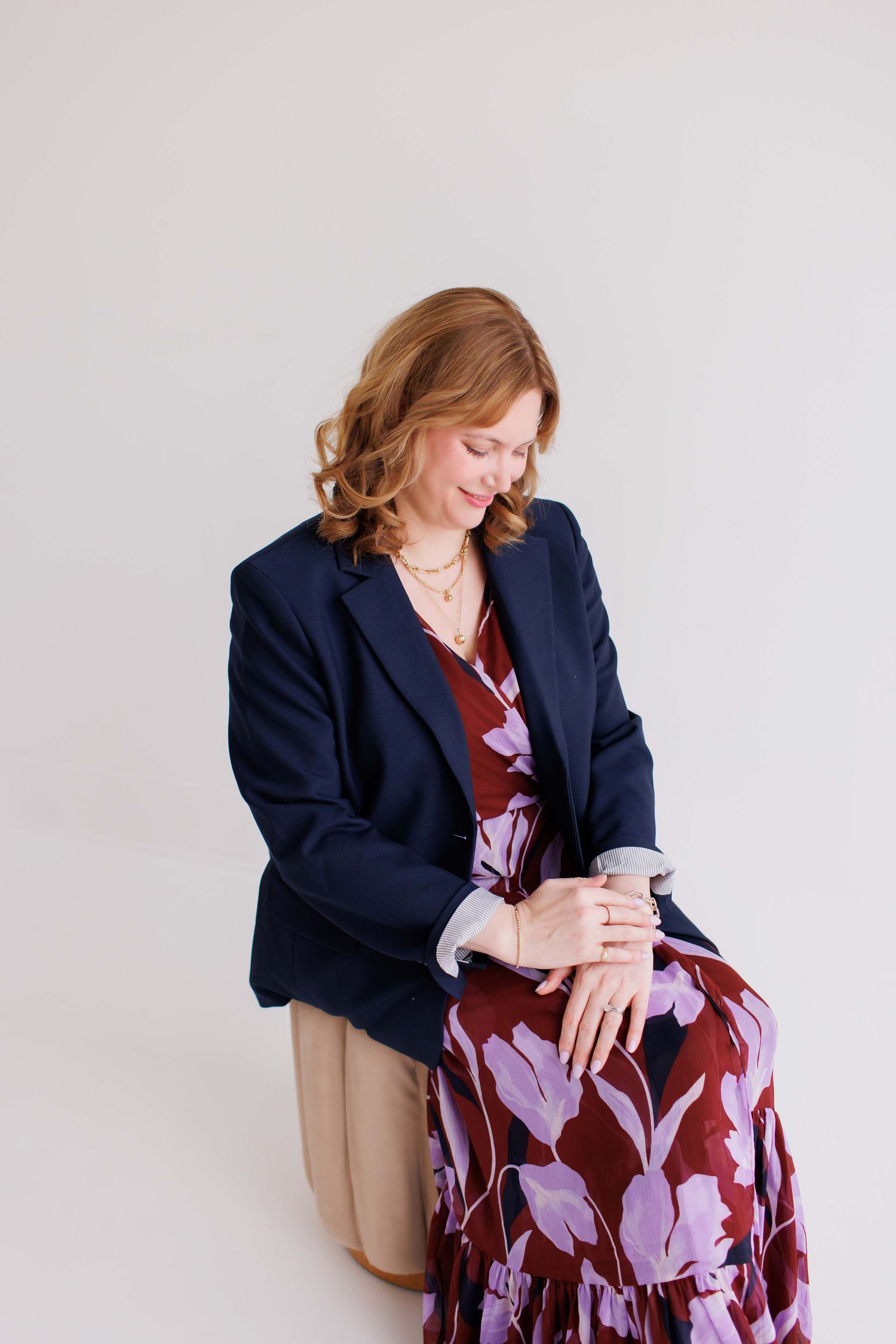 A person in a navy blazer and floral dress sits in a chair looking down at their phone.