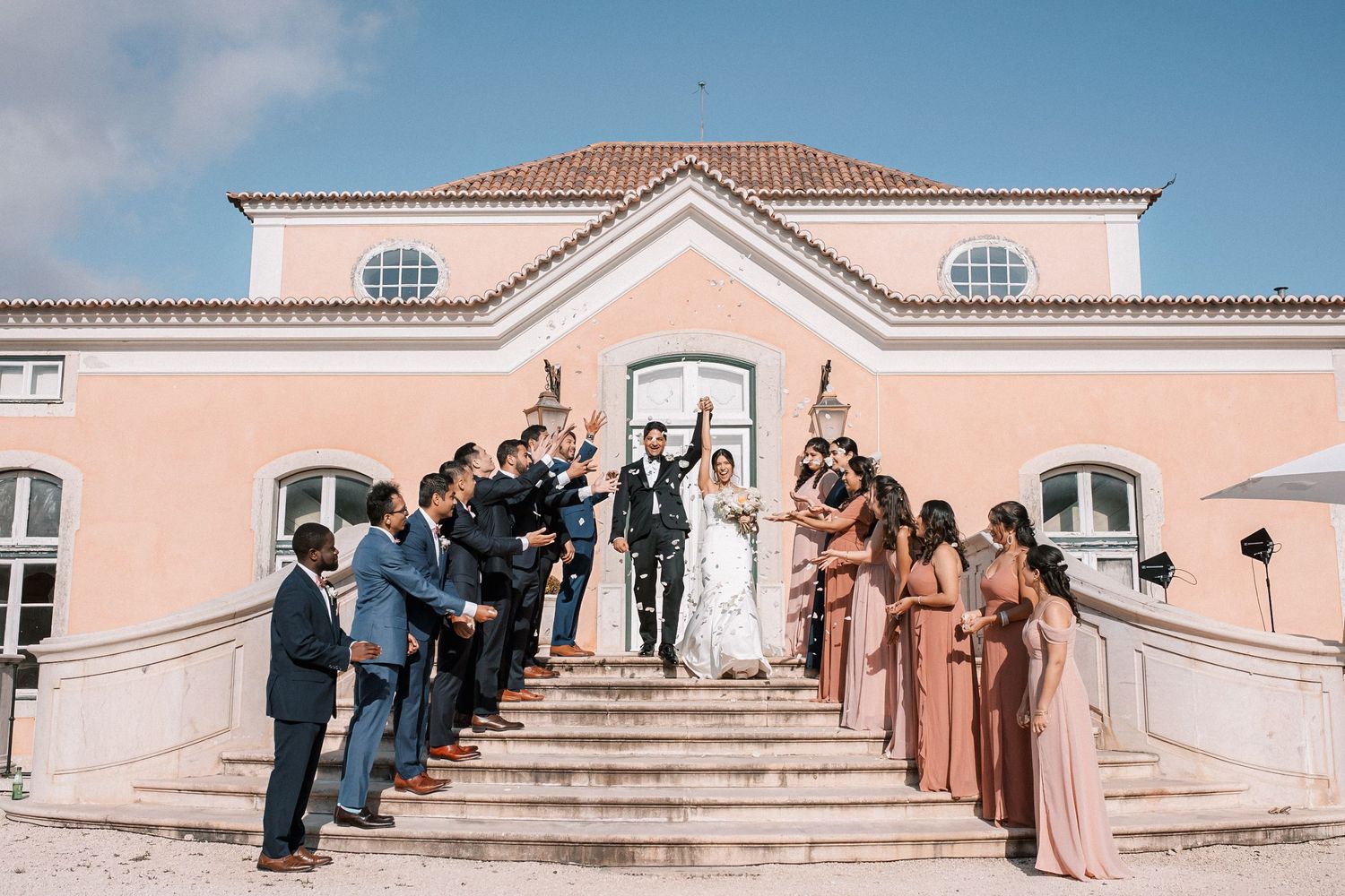 Bride and groom walking down the stairs of Palácio do Correio-Mor with bridal party throwing petals