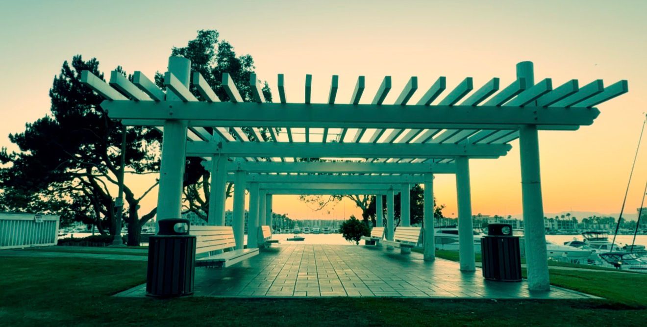 White pergola structure at waterfront park during sunset with trees and marina in background.