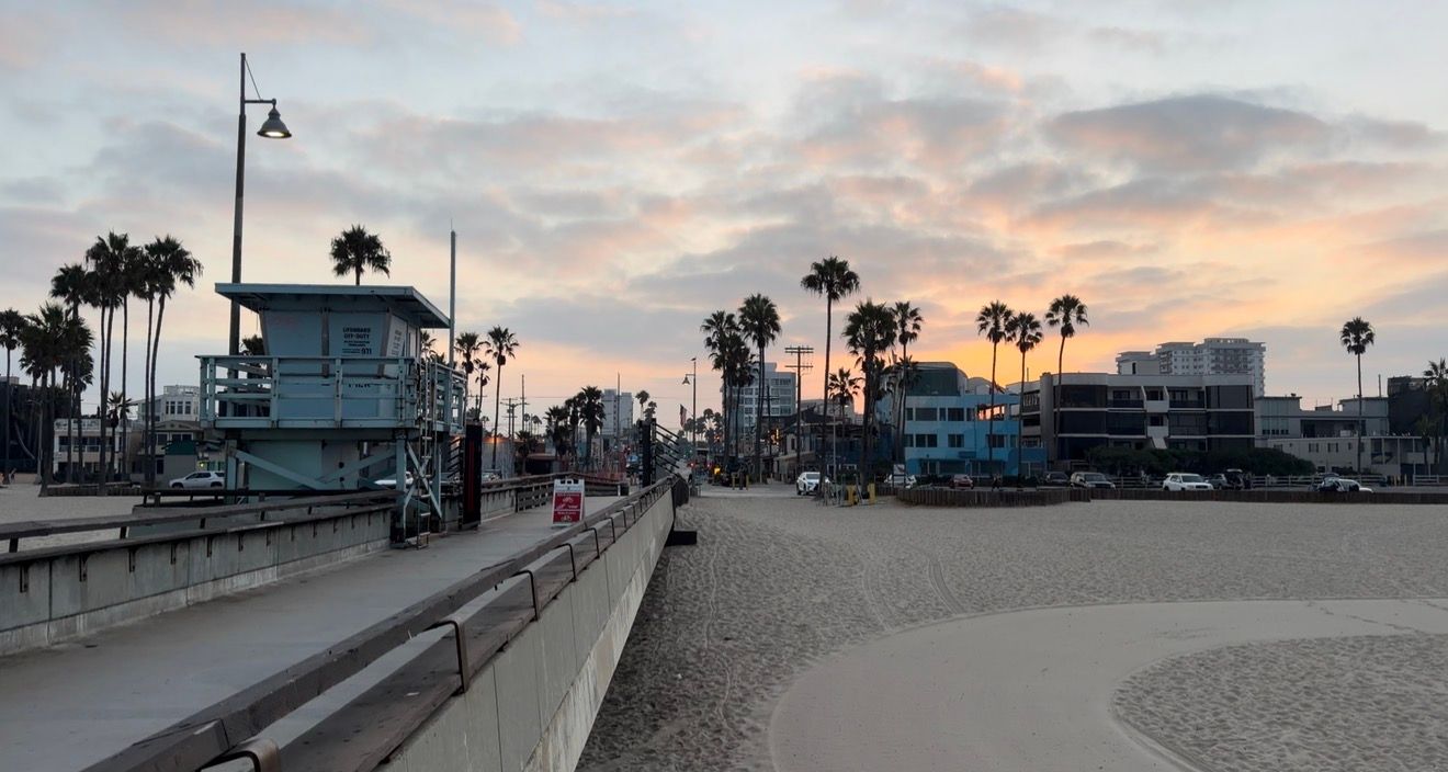Venice Beach boardwalk at sunset with palm trees, lifeguard tower, and colorful sky in Los Angeles, California.