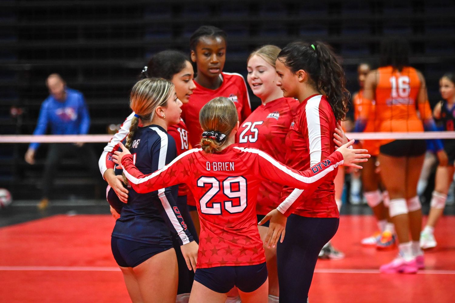 Female volleyball player #20 sets the ball during an indoor tournament match while teammate #33 prepares to spike.