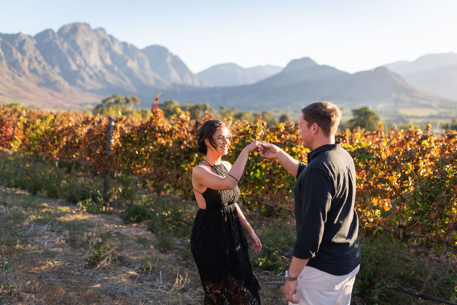 Couple dancing in a vineyard with autumn foliage and mountain backdrop in golden hour light.