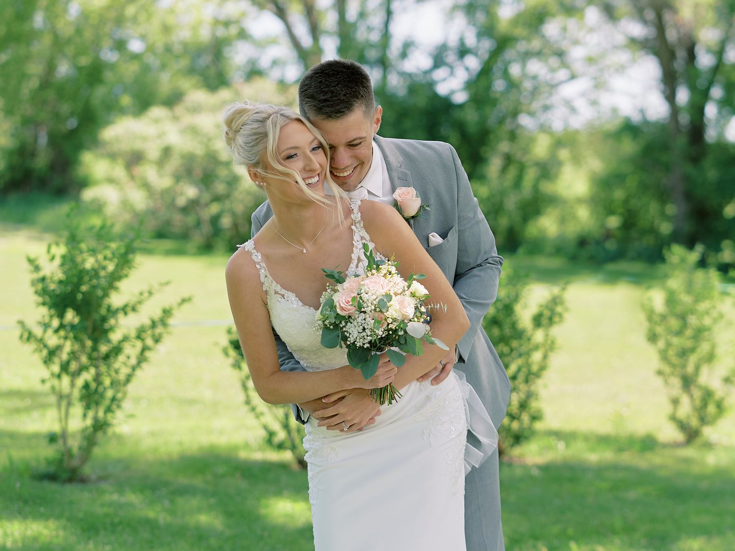 A wedding couple poses together outdoors, with the bride in a lace gown and groom wearing a yellow tie.