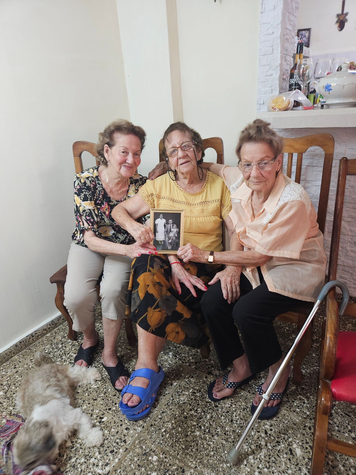 Three sisters holding a restored photo of the older sister with their parents.