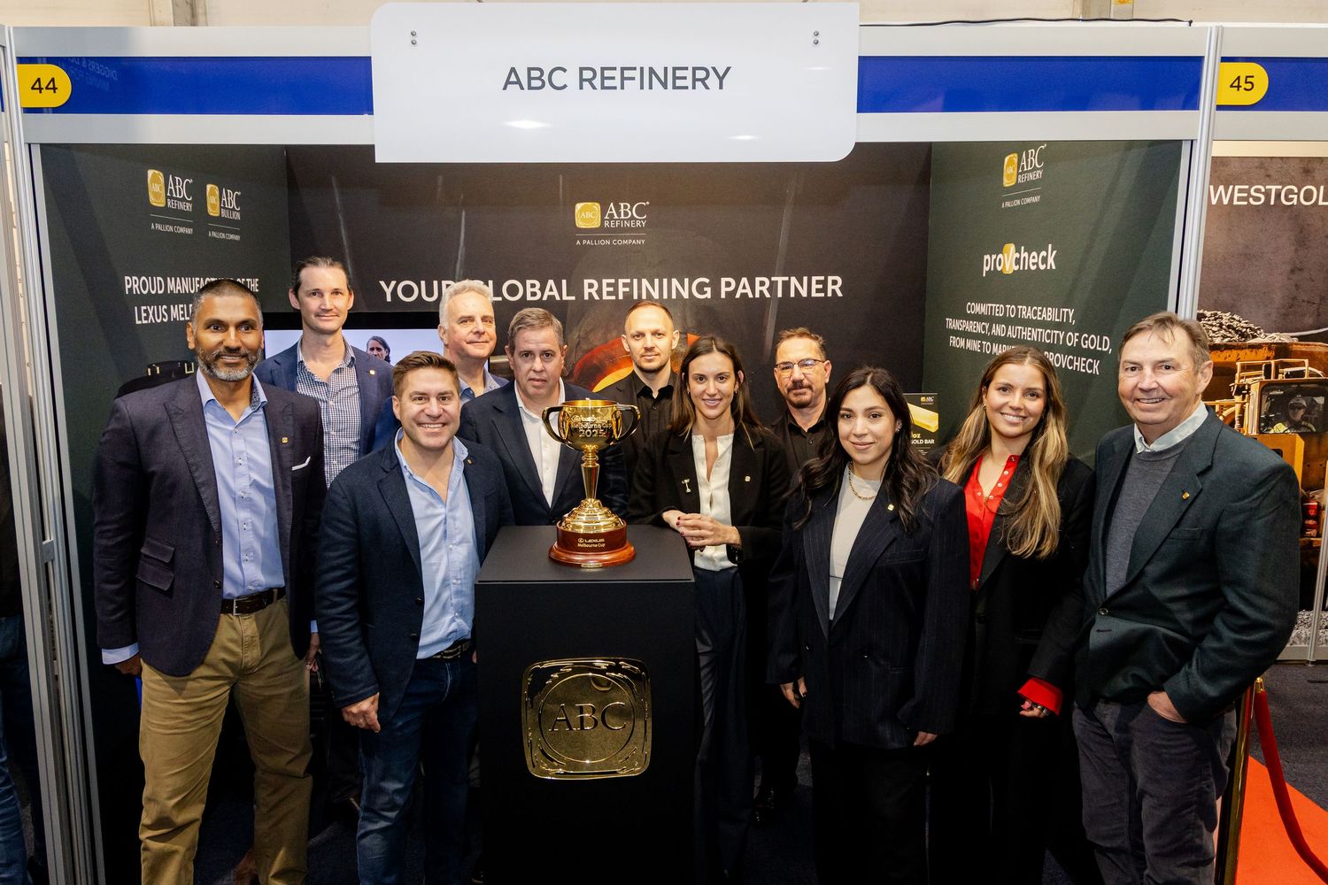 Five professionals smile at an ABC Global Refining Partner trade show booth with gold branding and display materials.
