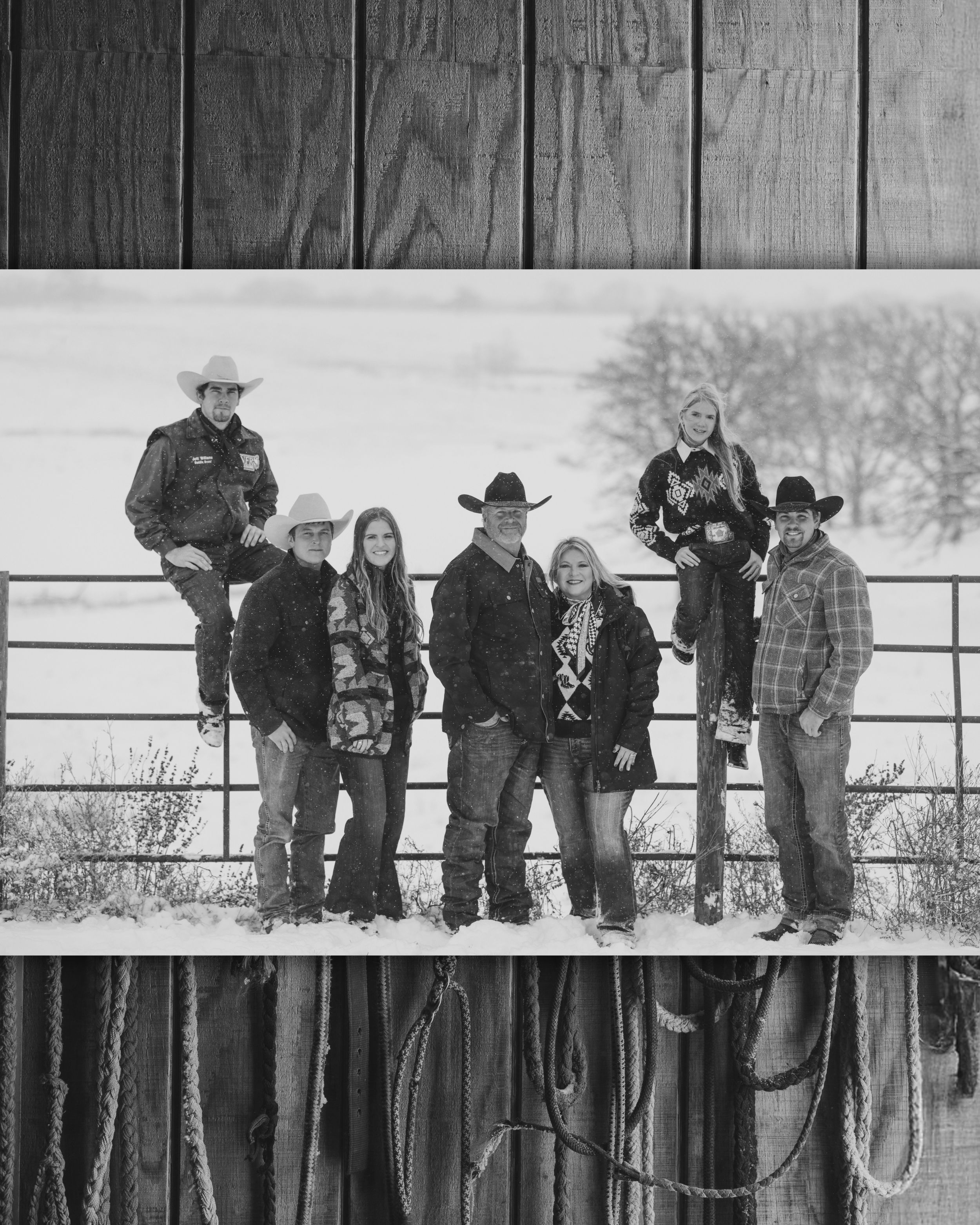 Black and white photo of six people in cowboy hats posing on a ranch fence in a snowy winter landscape.