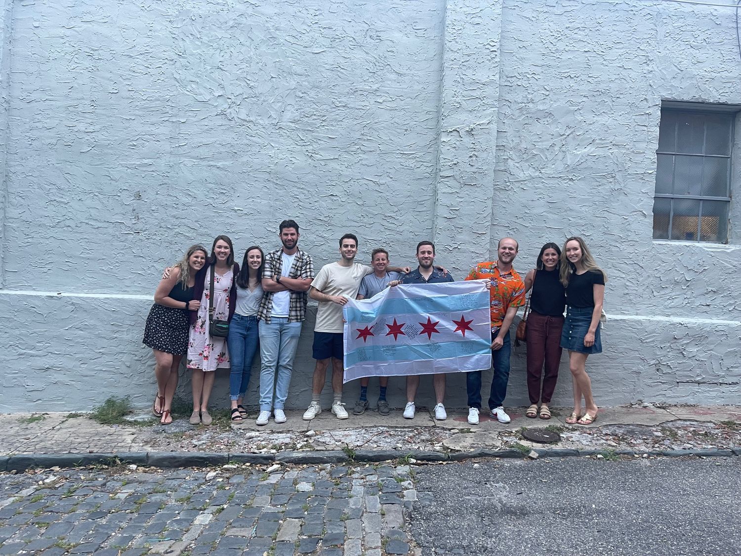 Group of friends posing with Chicago city flag in front of a white brick wall outdoors | Sydney Allen Photography
